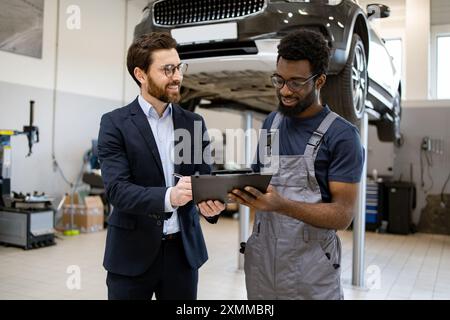 Mechaniker und Geschäftsmann diskutieren über Autowartung in der Garage Stockfoto
