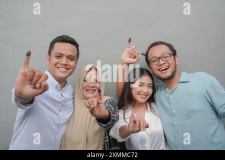 Porträt einer aufgeregten indonesischen Familie, die den kleinen Finger zeigt, der in violette Tinte getaucht ist, nachdem er für die Parlamentswahlen oder Pemilu für den Präsidenten und die Regierung gestimmt hat Stockfoto