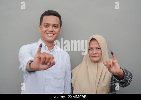 Porträt einer aufgeregten indonesischen Familie, die den kleinen Finger zeigt, der in violette Tinte getaucht ist, nachdem er für die Parlamentswahlen oder Pemilu für den Präsidenten und die Regierung gestimmt hat Stockfoto