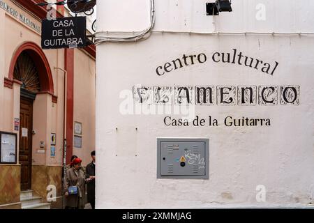 Sevilla, Spanien. 7. Februar 2024 - Schild des Centro Cultural Flamenco „Casa de la Guitarra“ an einer Wand gemalt, mit Menschen auf der Straße Stockfoto