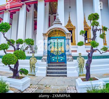 Die farbenfrohe Seitentür zu Ubosot von Wat Suthat mit zwei Wächtern, Bangkok, Thailand Stockfoto