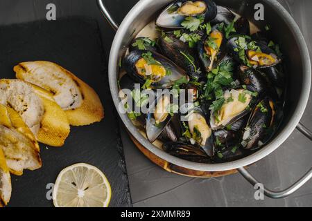 Muscheln in Weißwein mit Petersilie, gerösteten Baguetteschnitten und Zitrone auf einem grauen Tisch. Ein traditionelles Gericht der mediterranen Küche. Hochwertige Fotos Stockfoto