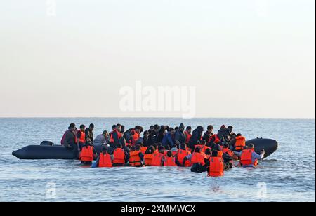 Eine Gruppe von Menschen, die als Migranten gelten, waten durch das Meer, um sich an Bord eines kleinen Bootes vor dem Strand in Gravelines, Frankreich, zu stürzen. Bilddatum: Montag, 29. Juli 2024. Stockfoto