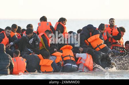 Eine Gruppe von Menschen, die als Migranten gelten, waten durch das Meer, um sich an Bord eines kleinen Bootes vor dem Strand in Gravelines, Frankreich, zu stürzen. Bilddatum: Montag, 29. Juli 2024. Stockfoto