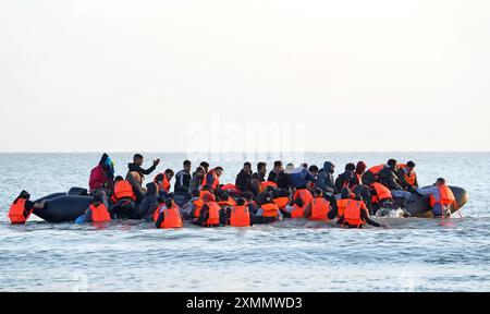 Eine Gruppe von Menschen, die als Migranten gelten, waten durch das Meer, um sich an Bord eines kleinen Bootes vor dem Strand in Gravelines, Frankreich, zu stürzen. Bilddatum: Montag, 29. Juli 2024. Stockfoto