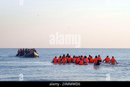 Eine Gruppe von Menschen, die als Migranten gelten, waten durch das Meer, um sich an Bord eines kleinen Bootes vor dem Strand in Gravelines, Frankreich, zu stürzen. Bilddatum: Montag, 29. Juli 2024. Stockfoto