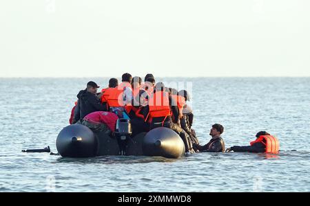 Eine Gruppe von Menschen, die als Migranten gelten, waten durch das Meer, um sich an Bord eines kleinen Bootes vor dem Strand in Gravelines, Frankreich, zu stürzen. Bilddatum: Montag, 29. Juli 2024. Stockfoto