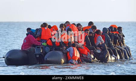 Eine Gruppe von Menschen, die als Migranten gelten, waten durch das Meer, um sich an Bord eines kleinen Bootes vor dem Strand in Gravelines, Frankreich, zu stürzen. Bilddatum: Montag, 29. Juli 2024. Stockfoto