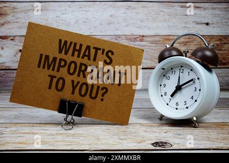 Was ist Ihnen wichtig? Text auf Papierkarte mit Wecker auf hölzernem Hintergrund Stockfoto