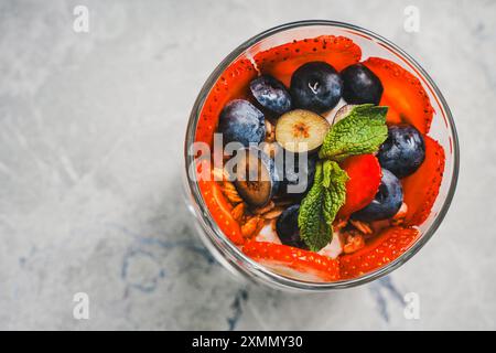 Beere leichtes Dessert zum Frühstück im Glas mit Erdbeeren, Heidelbeeren, Minze und Joghurt auf hellem Hintergrund. Nahaufnahme. Leerzeichen für Text. Kopieren Sie ein Spa Stockfoto
