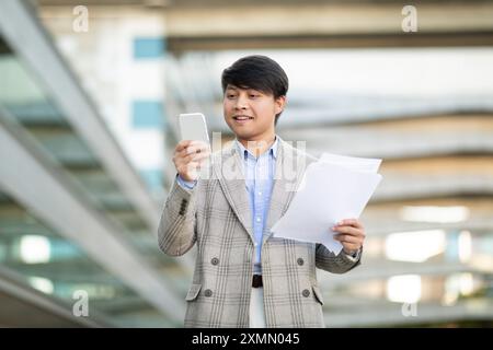Geschäftsmann, der Smartphone nutzt und Dokumente in der Stadt hält Stockfoto