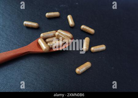 Braune Arzneimittelkapseln in einem Holzlöffel und einige verstreut mit Nahsicht auf schwarzem Hintergrund. Stockfoto