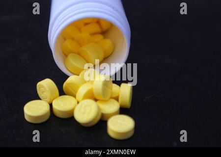 Gelbe Arzneimitteltabletten oder Vitamin-C-Medikamente, die aus der Flasche verschüttet werden, aus der Nähe. Stockfoto