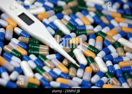 Digitalthermometer und bunte Pillen, Variation der Medikamente in Kapseln. Horizontaler Hintergrund für Antipyretika oder Antibiotika Stockfoto