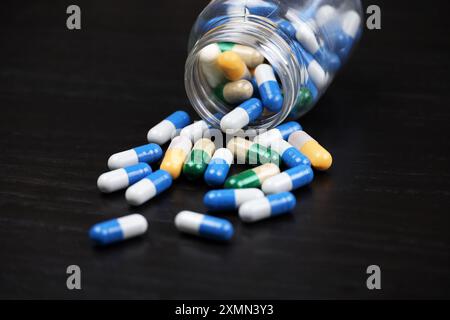 Pillen auf einem schwarzen Holztisch, Medikamente in bunten Kapseln, die aus einer Flasche verstreut sind. Hintergrundinformationen zu Pharmazie, Antibiotika, Vitaminen Stockfoto