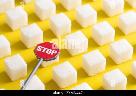 Zuckerwürfel und Stoppschild auf gelbem Hintergrund, Konzeptbild Stockfoto