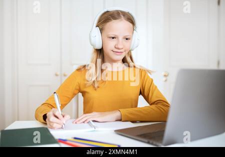 Teen Girl macht Notizen, während er einen Laptop und Kopfhörer benutzt Stockfoto