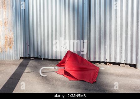 Gebrochener roter Regenschirm auf dem Boden in einer Stadtstraße, mit verschlossenem Hintergrund Stockfoto