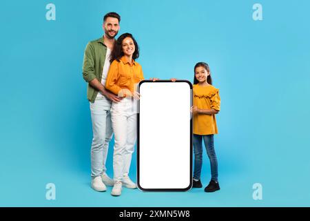 Happy Family mit großem Smartphone mit leerem Bildschirm auf Blau Stockfoto