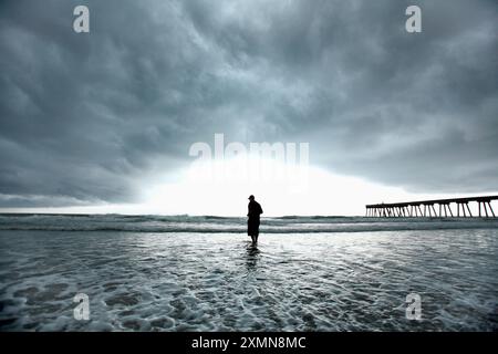 Ein Mann fischt mit einem Netz unter stürmischem, bewölktem Himmel in den Gewässern von Wrightsville Beach. Stockfoto