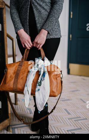 Eine Frau, die eine braune Ledertasche mit einem floralen Schal hält. Stockfoto