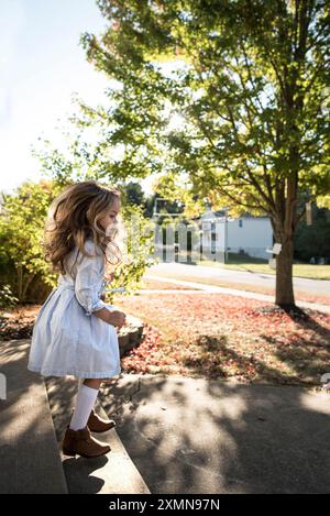 Kleines Mädchen, lange blonde Locken, die in Kleid und Stiefeln springen Stockfoto