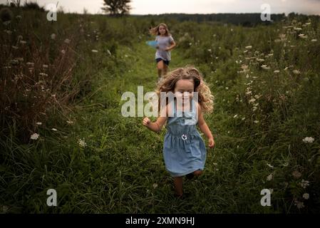 Junge Schwestern, die im Sommer durch das Wildblumenfeld rennen Stockfoto