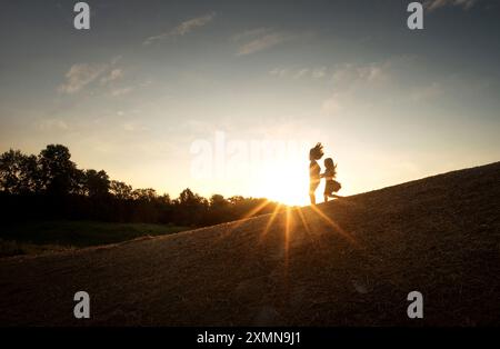 Junge Schwestern, die durch den Sonnenaufgang den Berg hinunter laufen Stockfoto