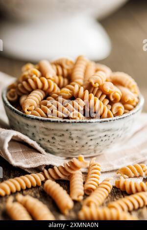 Ungekochte Vollkornnudeln. Rohe Fusilli-Pasta in einer Schüssel auf einem Holztisch. Stockfoto