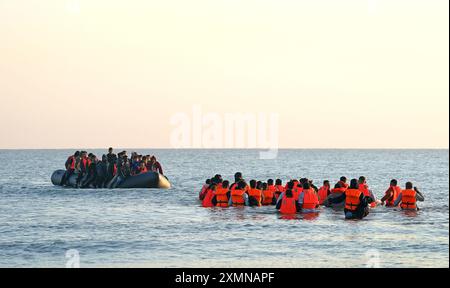 Eine Gruppe von Menschen, die als Migranten gelten, waten durch das Meer, um sich an Bord eines kleinen Bootes vor dem Strand in Gravelines, Frankreich, zu stürzen. Bilddatum: Montag, 29. Juli 2024. Stockfoto