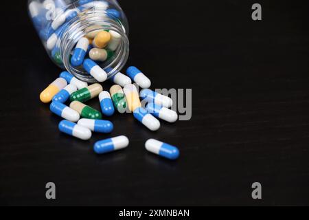 Pillen auf einem schwarzen Holztisch, Medikamente in bunten Kapseln, die aus einer Flasche verstreut sind. Hintergrundinformationen zu Pharmazie, Antibiotika, Vitaminen Stockfoto