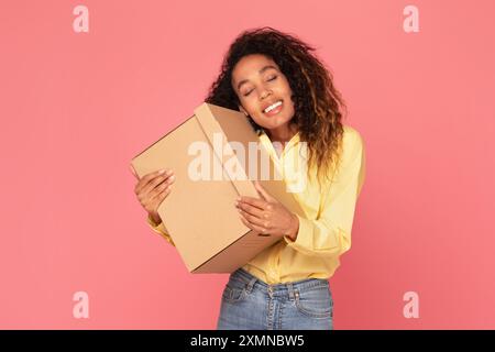 Junge Frau, Die Pappschachtel Vor Rosa Hintergrund Hält Stockfoto