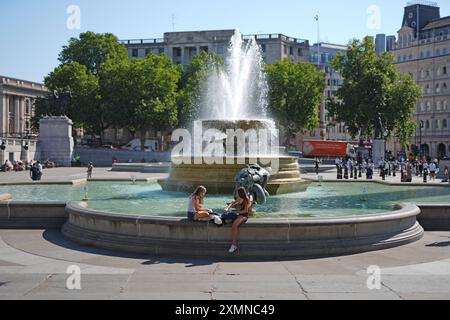 Die Leute sitzen an den Springbrunnen am Trafalgar Square, im Zentrum von London. Hohe Temperaturen könnten zu einer offiziellen Hitzewelle führen, wobei ein Großteil Großbritanniens in den nächsten Tagen „sehr warmes, lokal heißes Wetter“ genießen wird. Bilddatum: Montag, 29. Juli 2024. Stockfoto