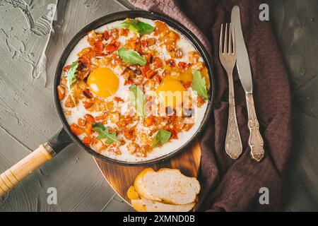 Rührei mit Tomaten, Paprika, Schalotten und Speck in einer gusseisernen Pfanne mit Brotscheiben. Köstliches, nahrhaftes und gesundes Frühstück GRA Stockfoto