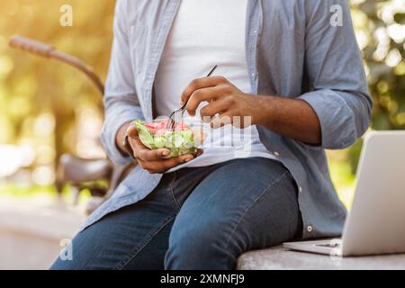 Unerkennbarer Afrikanischer Mann, Der Salat Isst Und Im Park Gesundes Mittagessen Im Freien Hat Stockfoto