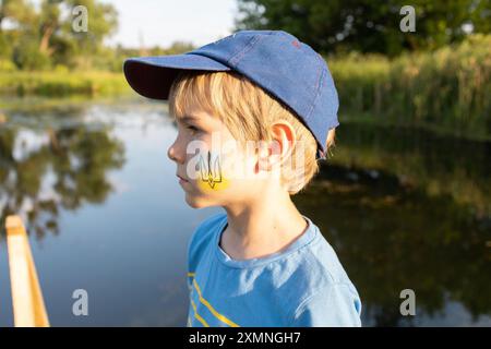 Trauriger Junge mit einem nationalen Symbol auf der Wange - ein Dreizack auf blauem und gelbem Hintergrund. Ukrainisches patriotisches Konzept. Stoppt den Krieg. Traum von V Stockfoto