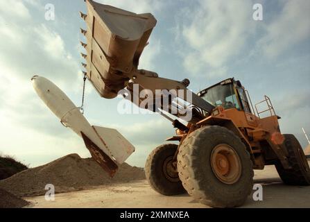 Ein Bagger, der eine Bombe aus seinem BucketA Digger trägt eine ausgegrabene Rakete, die an den Eimer gekettet ist, auf einer Baustelle in Sussex, England, Großbritannien 1999 Bild von Roger Bamber Stockfoto