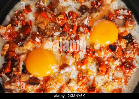 Rührei mit Tomaten, Paprika, Schalotten und Speck in einer gusseisernen Pfanne mit Brotscheiben. Köstliches, nahrhaftes und gesundes Frühstück GRA Stockfoto