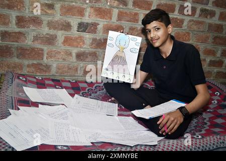 Ein glücklicher Schuljunge zeigt seine wunderschöne Zeichnung vor der Kamera, verstreute Notizbuchseiten und Backsteinmauern Stockfoto