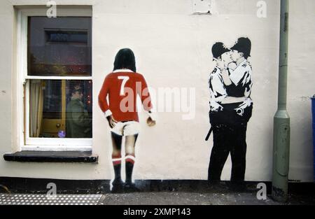 25. Dezember 2005: Das berühmte Graffiti-Bild der küssenden Coppers wurde 2004 von dem Underground-Künstler Banksy auf eine Pub-Wand in Brighton gesprüht. Es zeigt auch eine Rückansicht des Fußballers George Best neben den zwei küssenden schwulen Polizisten. Das beste Bild wurde kurz nach seinem Tod im November 2005 hinzugefügt. Die Bilder wurden an der Seite eines Prince Albert Pubs in Brighton Sussex England gesprüht, aber die Polizisten wurden entfernt und 2008 für 575 US-Dollar verkauft. Stockfoto