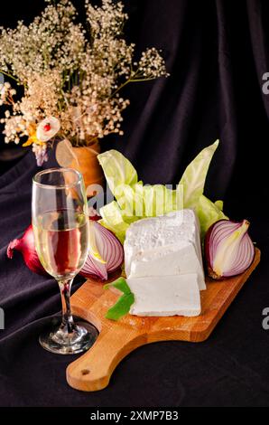 Stillleben mit Käse, Zwiebeln und einem Glas Weißwein auf schwarzem Hintergrund Stockfoto