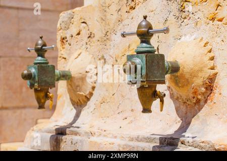 Zwei elegante Trinkwasserhähne mit grüner Patina an einer Steinmauer in Tarragona, Spanien Stockfoto