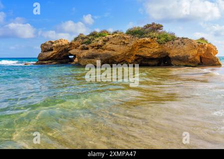 Atemberaubender Blick auf die Küste mit einem Felsvorsprung, umgeben von klarem Wasser und sanft plätschernden Wellen, unter einem teilweise bewölkten Himmel in Tarragona, Spanien Stockfoto