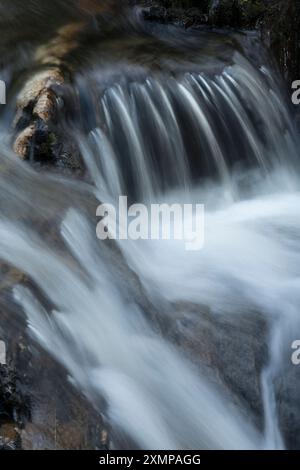 Abstraktes Detail des Wassers, das über Felsen in einem Gebirgsbach in der Nähe von Ballachulish, Glencoe, Schottland, Großbritannien fließt Stockfoto