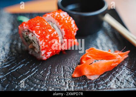 Japanisches Essen, Sushi-Brötchen auf einem schwarzen Teller mit Ingwer und Wasabi. Sushi-Brötchen mit Garnelen und Avacado, gebacken mit fliegenden Fischkaviar. Restaurantmänner Stockfoto