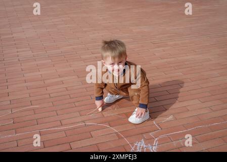 Kleiner Junge, der mit Kreide auf dem Bürgersteig kritzelte, Blick von oben Stockfoto