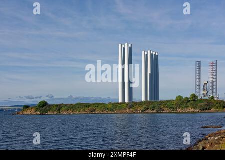 Windturbinentürme stehen aufrecht und warten auf den Weitertransport im Hafen von Dundee, mit einer Jack-up-Ölplattform im Hintergrund. Stockfoto