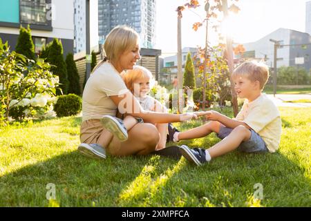 Mutter genießt Spielzeit mit ihren zwei Söhnen an einem hellen sonnigen Tag auf dem Spielplatz Stockfoto