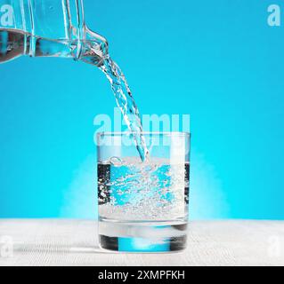 Wasser strömt in ein Glas auf blauem Hintergrund Stockfoto