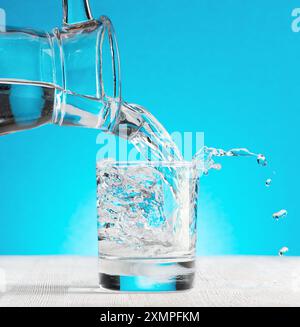 Wasser strömt in ein Glas auf blauem Hintergrund Stockfoto